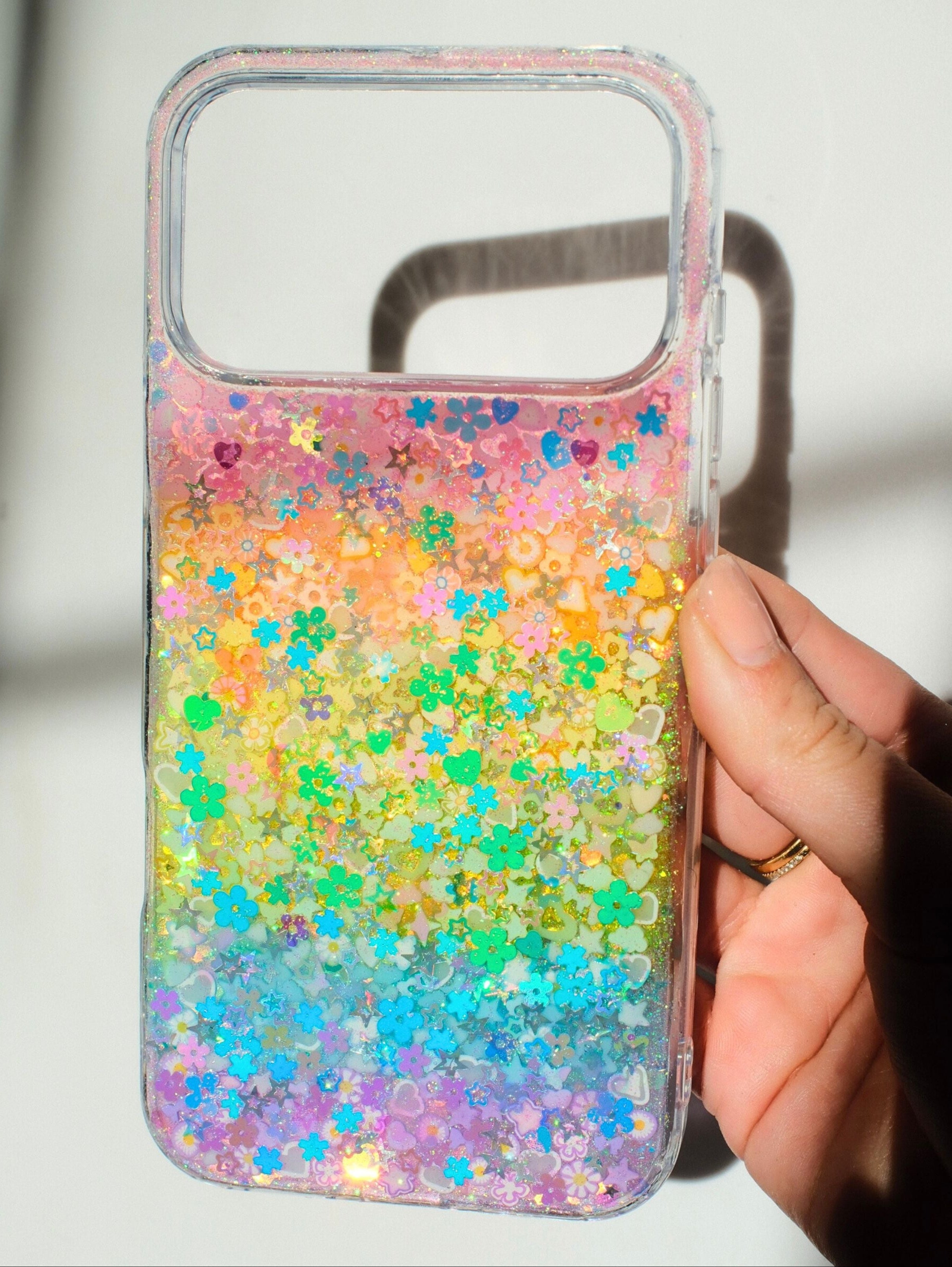 Colorful glittery phone case held by a hand against a neutral background