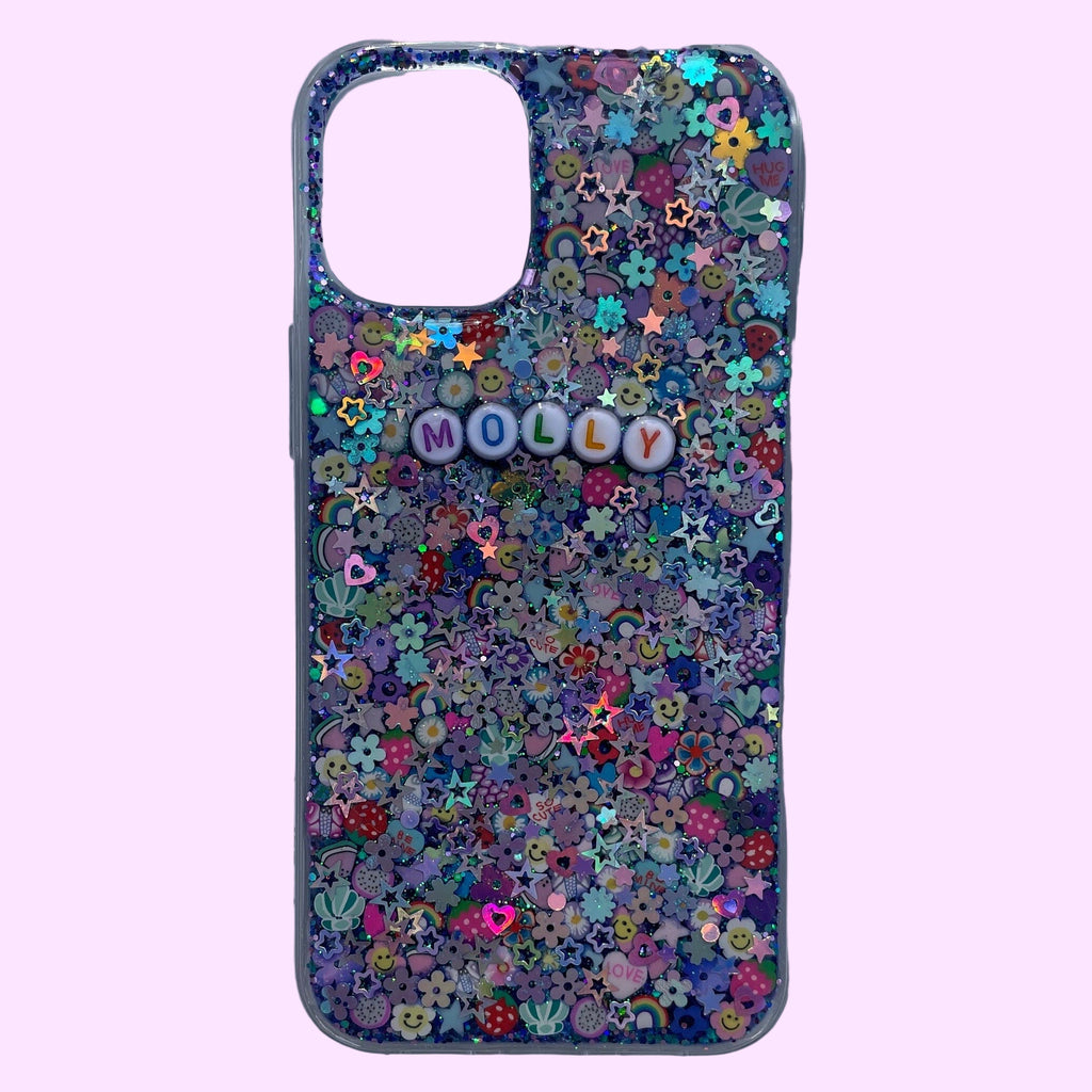 
A clear smartphone case featuring a maximalist, multi-colored design on a purple and teal glitter base. The back is densely packed with 3D charms, including strawberries, rainbow arches, flowers, and holographic stars. White circular beads with multicolored letters are centered on the case, spelling out the name "MOLLY." The case is shown against a soft lavender background with a large rectangular camera cutout at the top.