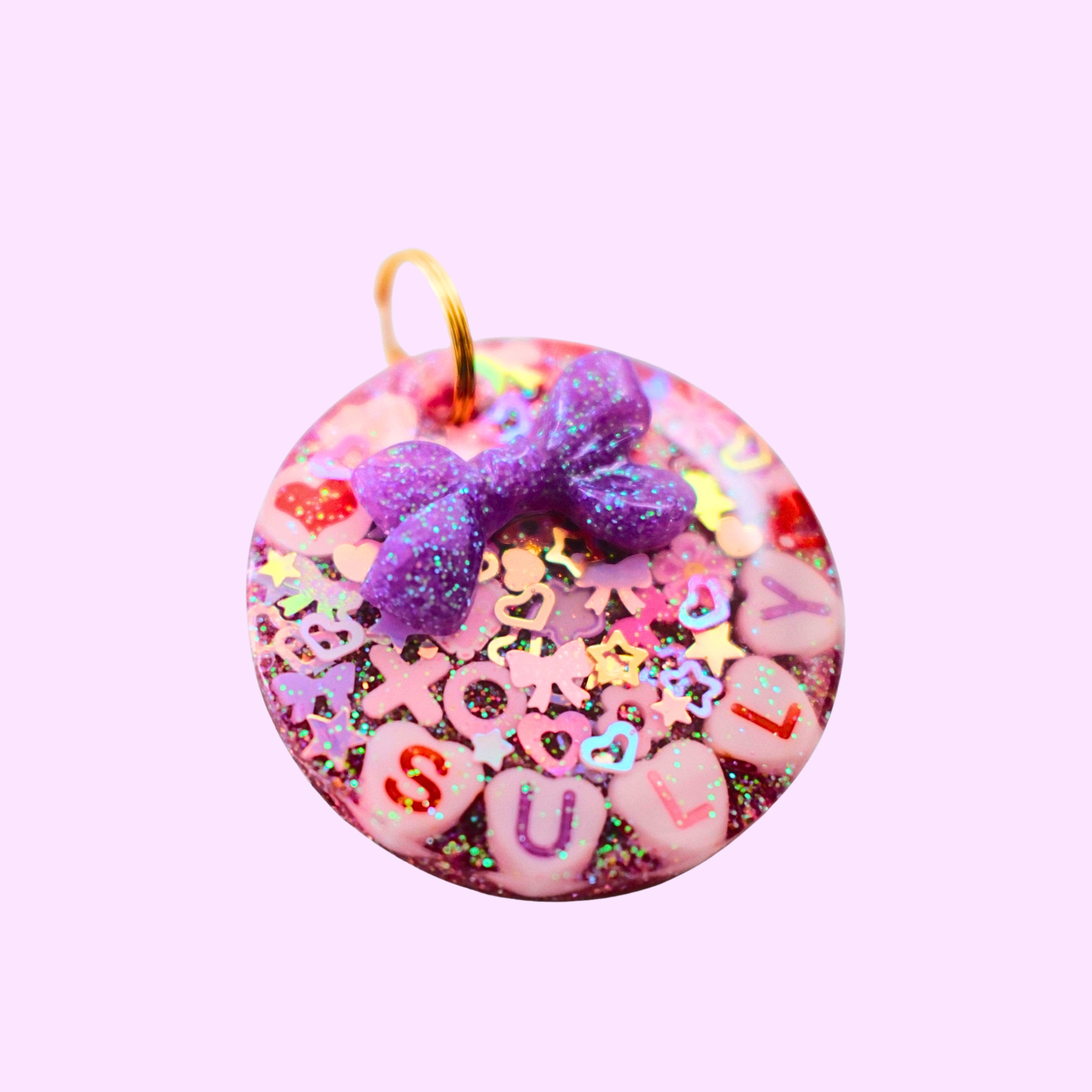 Circle-shaped pink and red Valentine-themed pet ID tag decorated with heart-shaped letter beads spelling the pet’s name and a 3D purple bow charm
