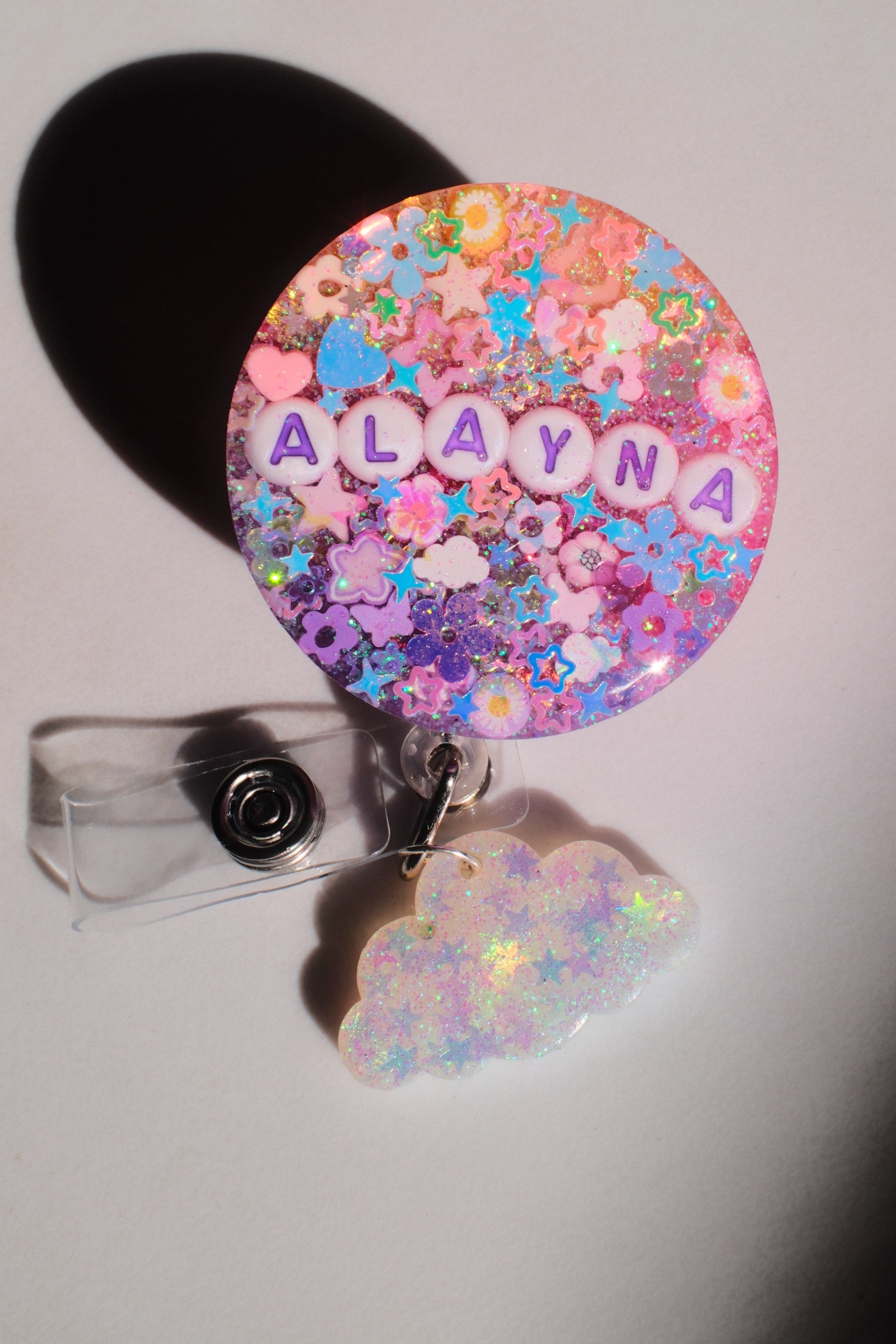 Colorful badge holder with floral design and 'Alaya' text on a light gray background