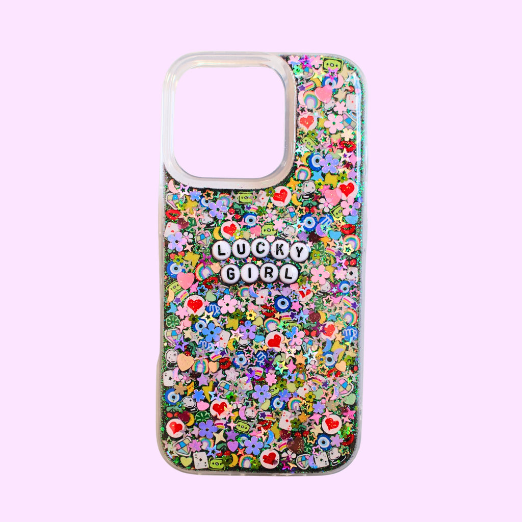 A clear phone case with a black sparkle resin base topped with a rainbow assortment of polymer clay slices with black letter beads that say "lucky girl" on a soft pink background