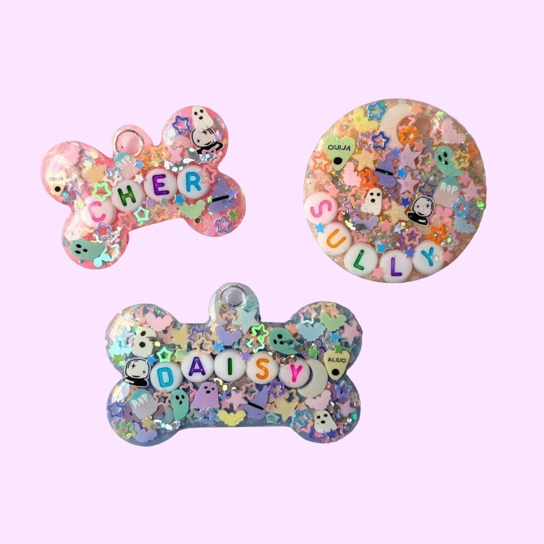 Three colorful bone-shaped name tags with pastel designs and letters on a white background