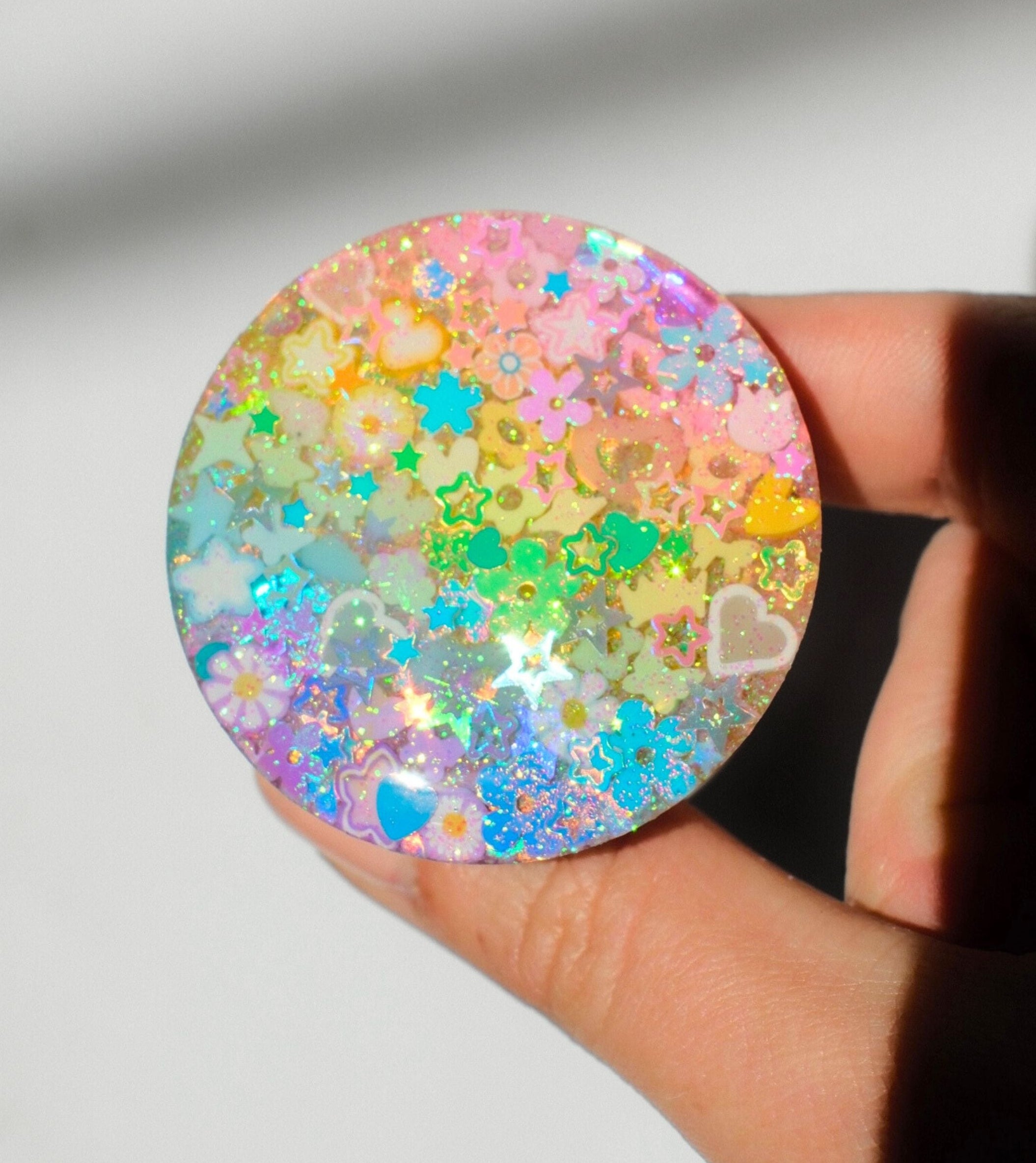 Hand holding a round, multicolored glittery object against a plain background